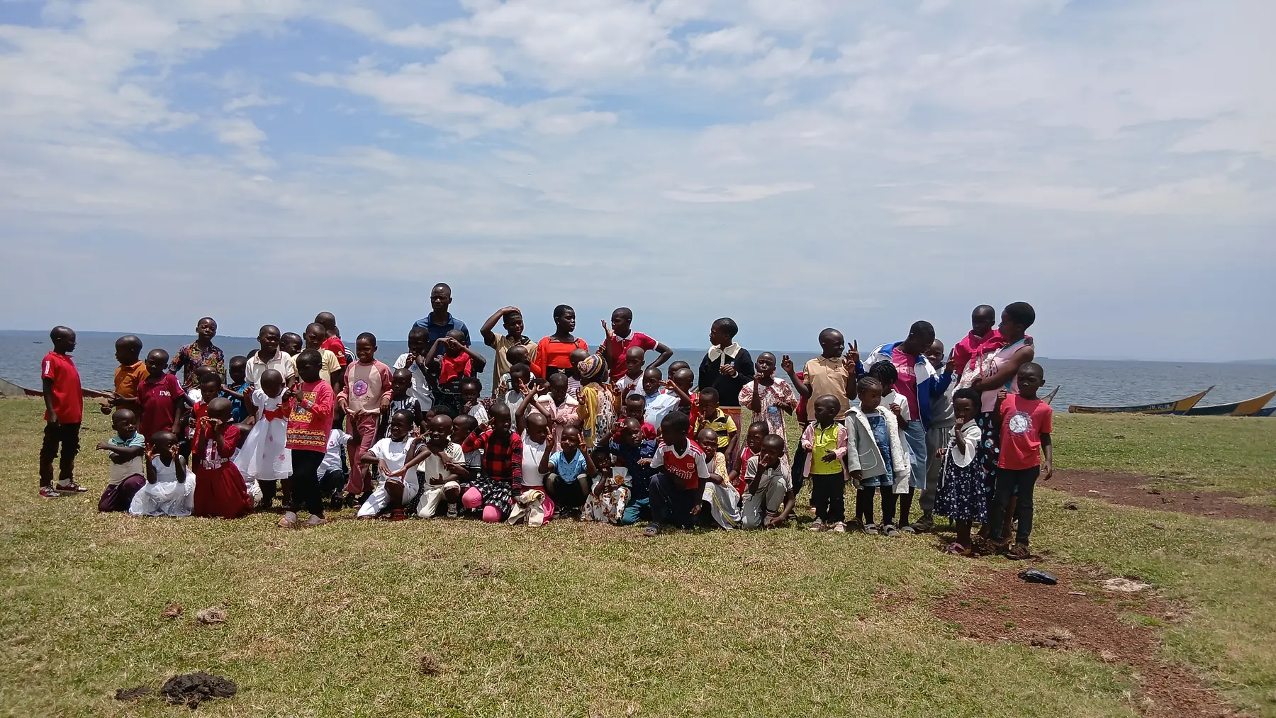 A large group of children and adults gathered on the grass by the Lake Victoria shoreline