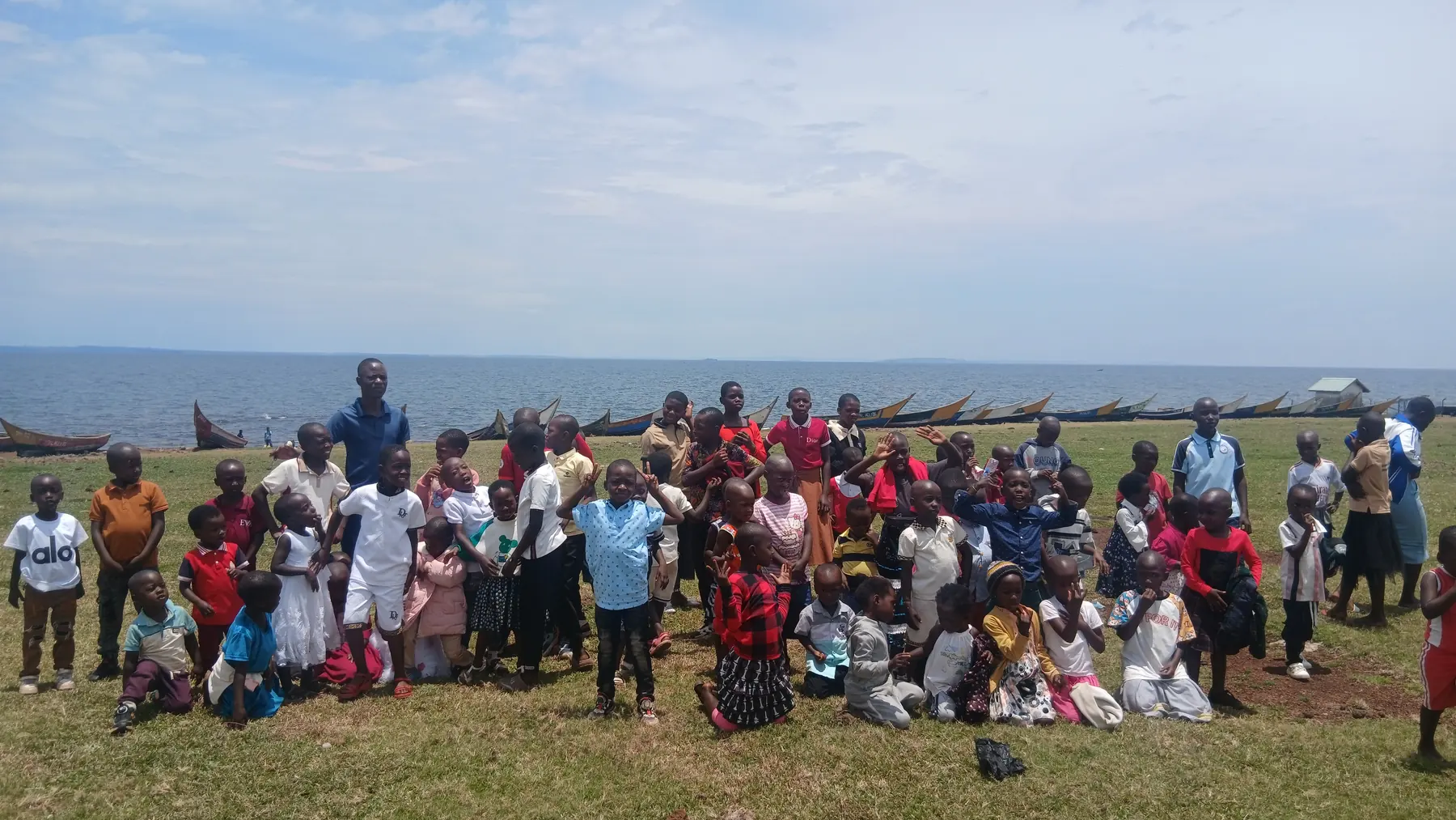 Children and adults posing together outdoors, with the lake and fishing boats behind them