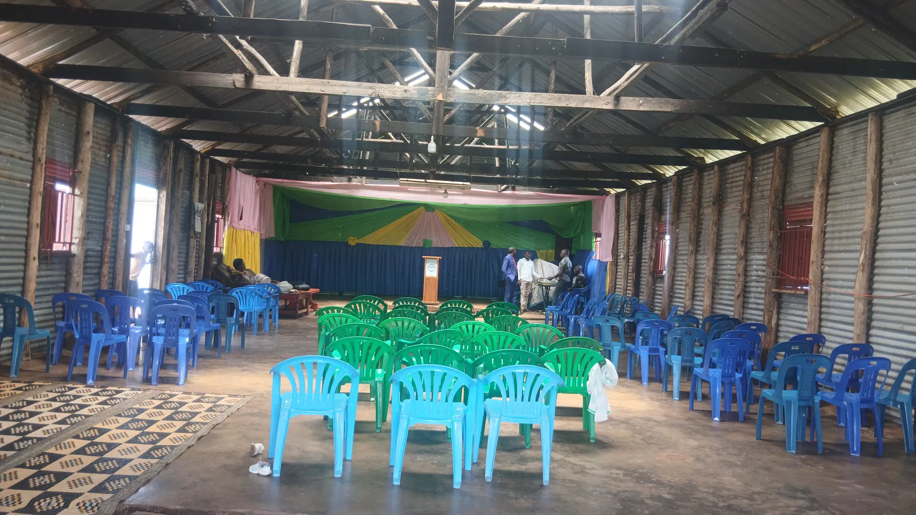 The inside of a church hall set with rows of blue and green plastic chairs facing a colourful stage