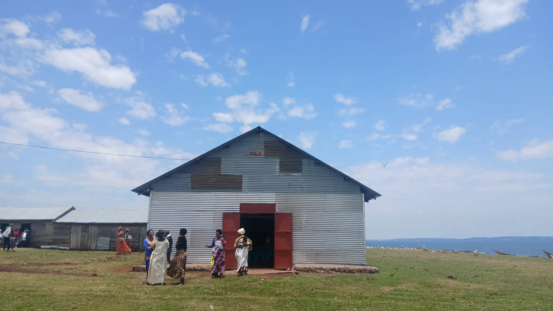 A metal-clad hall with a red door under a wide blue sky, with people gathered outside