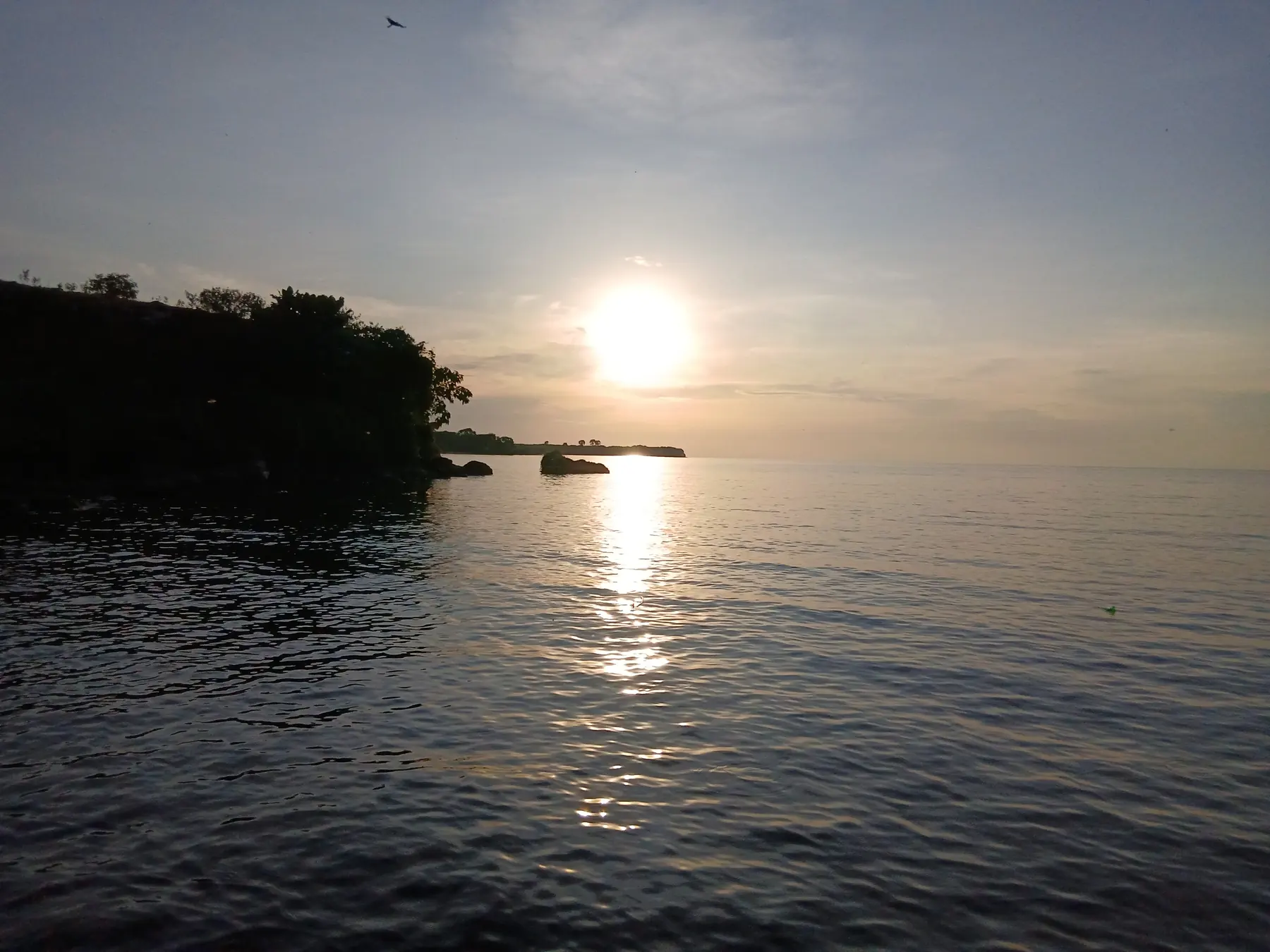 The sun setting over Lake Victoria beside a wooded island headland